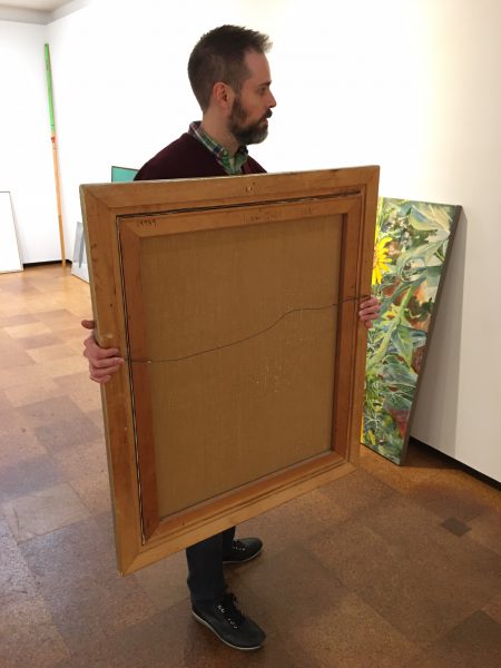This is the proper way to carry most any small to medium sized two-dimensional work of art. It faces the man carrying the artwork and it is being held with two hands on each side of the painting keeping the artwork's orientation up. Notice that it is being carried slightly to the side so it does not restrict the man from seeing where he is going. Also, if for any reason the artwork is dropped, the man will not fall into the painting.