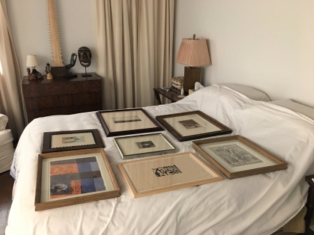 The bed in a spare bedroom is a great place to temporarily store small artworks. If they are to be covered, to keep dust off them, only use a thin transparent plastic drop cloth so it is obvious that there is art on the bed.  Be sure to keep pets out of the room.